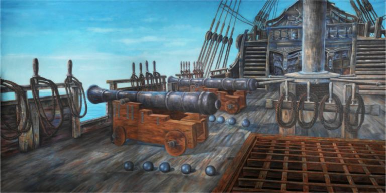 Wooden ship deck with cannons on wheeled carriages, cannonballs lined up, and ropes along the railing against a blue sky and sea backdrop.