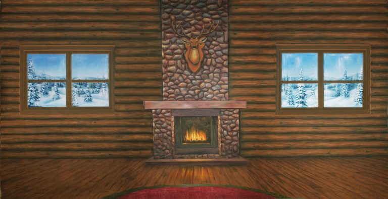 Cozy cabin interior with a stone fireplace and a deer head mantle, flanked by two snowy windows.