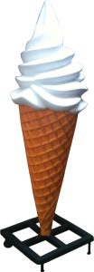 Soft-serve vanilla ice cream cone with a swirled white top, in a waffle cone mounted on a black metal stand.