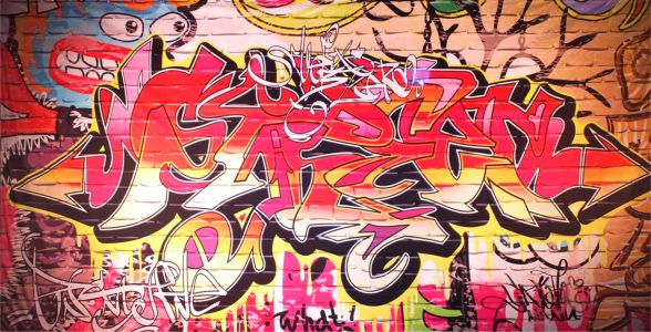 Vibrant wildstyle graffiti mural on a brick wall with overlapping pink, red, yellow letters and black outlines.