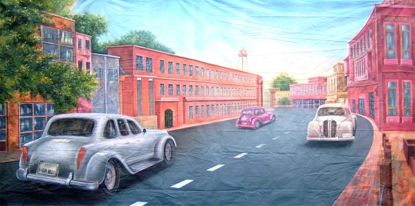 Pastel-colored city street mural with three vintage cars driving along a curved road under a blue sky, brick buildings on both sides.